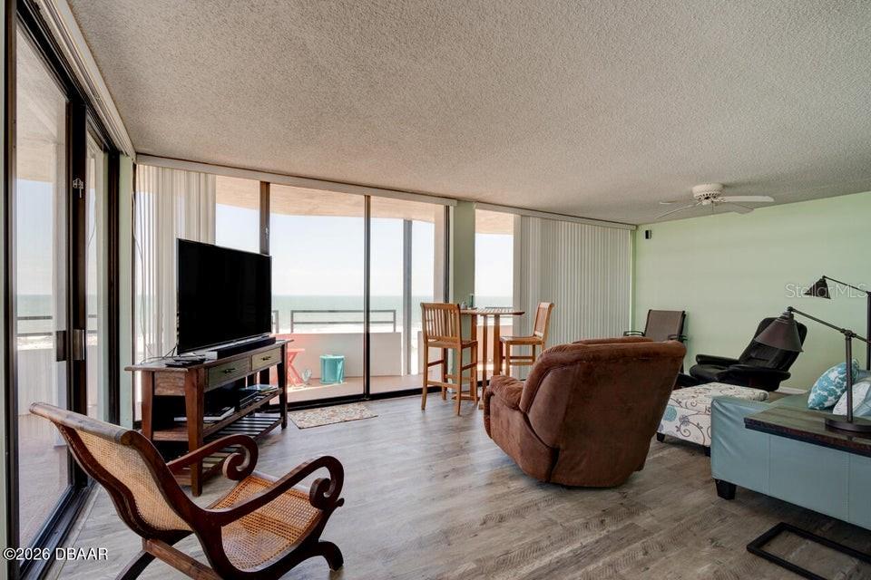 A living room with wood-look flooring, a brown recliner, and a balcony overlooking the ocean — 2828 N ATLANTIC AVENUE UNIT 701, DAYTONA BEACH, FL