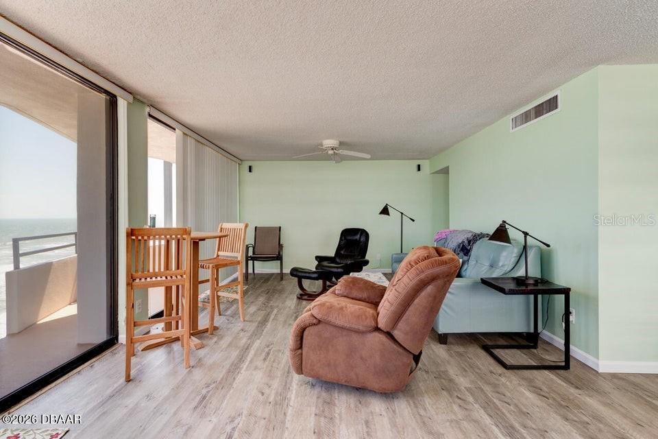 A living room features light green walls, wood-look flooring, a recliner, and a balcony view — 2828 N ATLANTIC AVENUE UNIT 701, DAYTONA BEACH, FL
