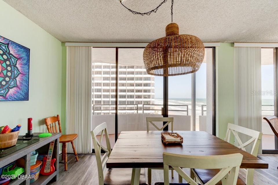 A dining area features a wooden table, woven pendant light, and sliding doors overlooking the ocean — 2828 N ATLANTIC AVENUE UNIT 701, DAYTONA BEACH, FL
