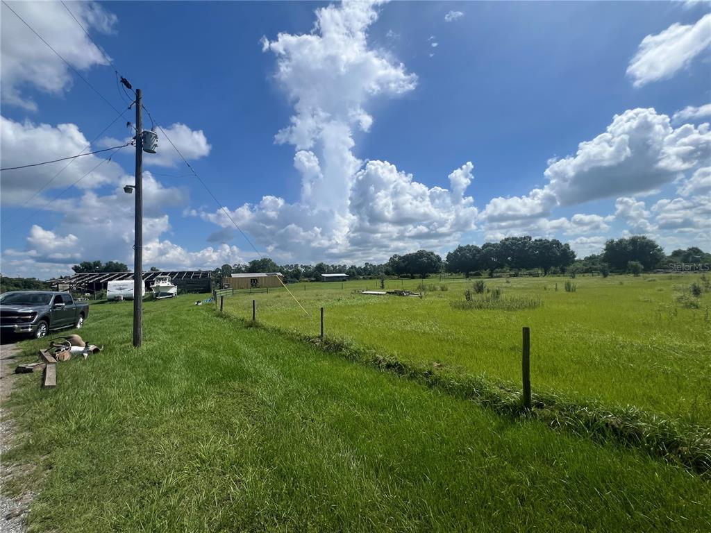 A grassy field features a utility pole, a parked truck, and several outbuildings under a sky — 8755 WAUCHULA ROAD, MYAKKA CITY, FL