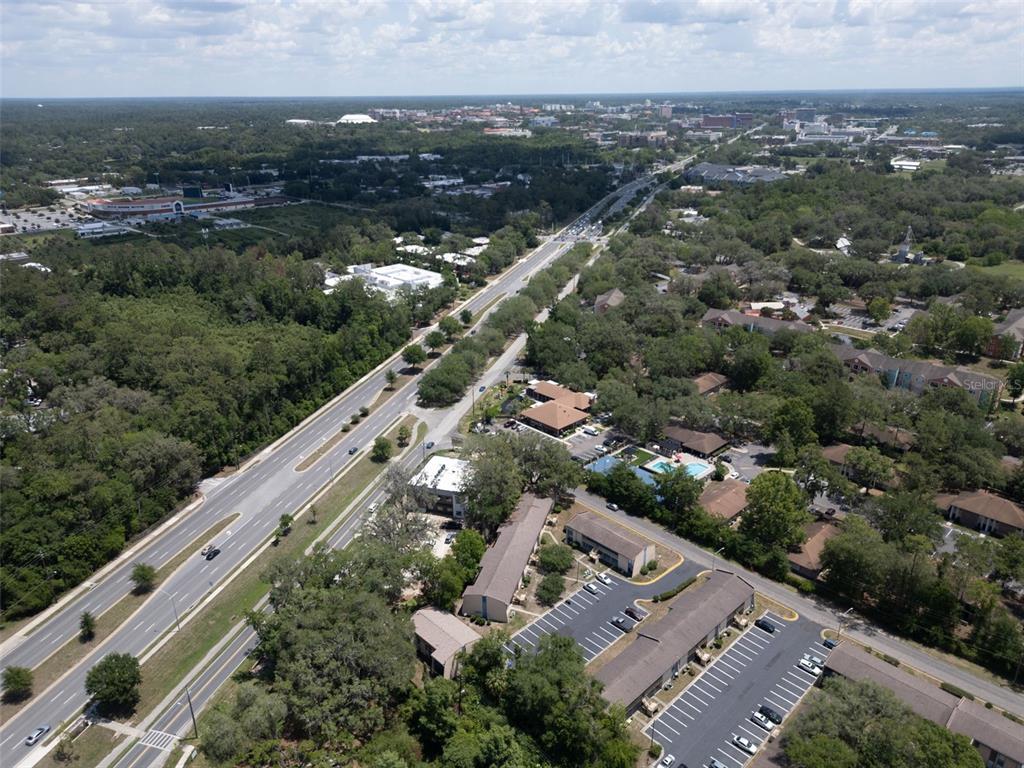 An aerial view shows a multi-lane road running through a wooded area with nearby buildings — 2811 SW ARCHER ROAD UNIT C18, GAINESVILLE, FL