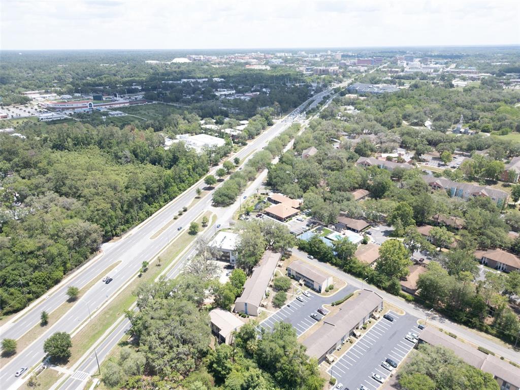 An aerial view shows a multi-lane highway running through a wooded area with nearby buildings — 2811 SW ARCHER ROAD UNIT C18, GAINESVILLE, FL