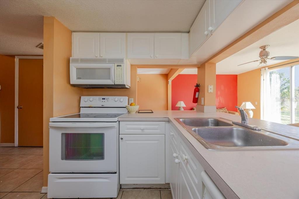A kitchen features white appliances, white cabinets, and a double-basin sink with a pass-through window — 203 COCO PLUM DRIVE Main Unit, DAVENPORT, FL