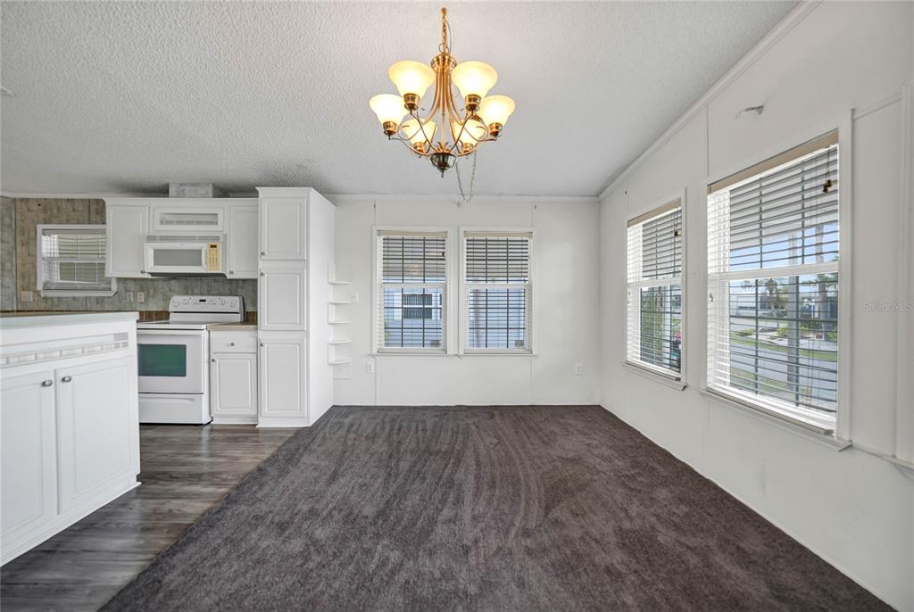 A dining area with dark carpet, white walls, a chandelier, and an adjacent white kitchen — 2100 KINGS HWY UNIT 206, PORT CHARLOTTE, FL