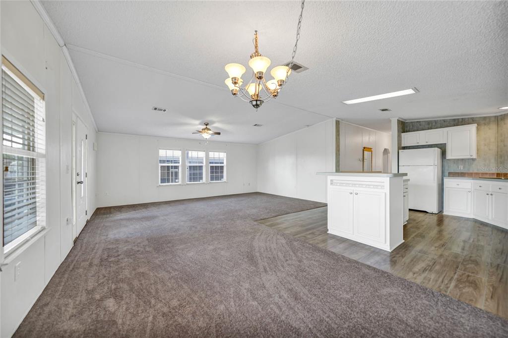 An open-concept living room and kitchen featuring gray carpeting, white cabinetry, and a chandelier — 2100 KINGS HWY UNIT 206, PORT CHARLOTTE, FL