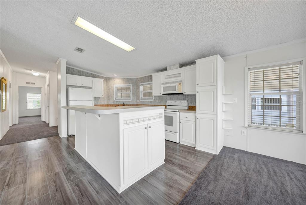 A kitchen with white cabinets, a central island, and wood-look flooring next to a carpeted area — 2100 KINGS HWY UNIT 206, PORT CHARLOTTE, FL