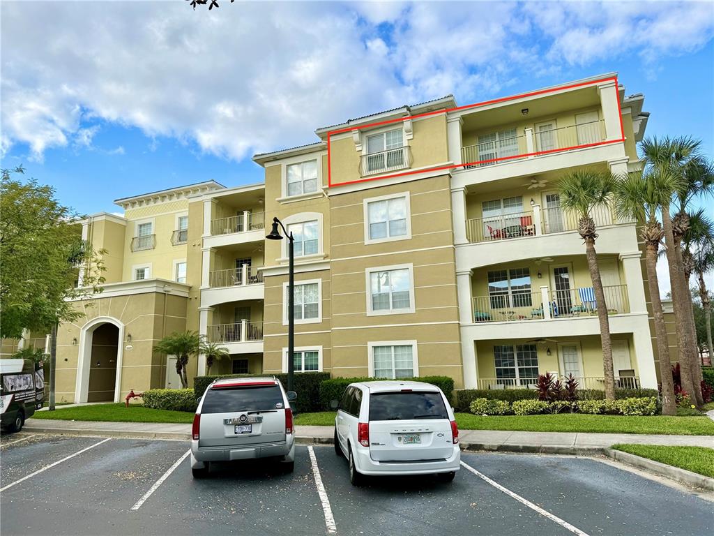 An exterior view of a multi-story apartment building with a red-outlined top-floor balcony — 5049 SHOREWAY LOOP UNIT 407, ORLANDO, FL