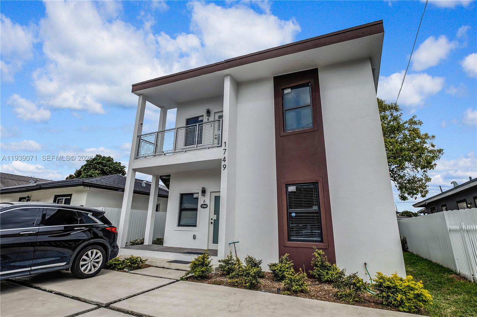 A two-story white building features a brown vertical accent, a balcony, and a concrete driveway — 1749 NW 64th St # A, Miami FL 33147, MIAMI, FL