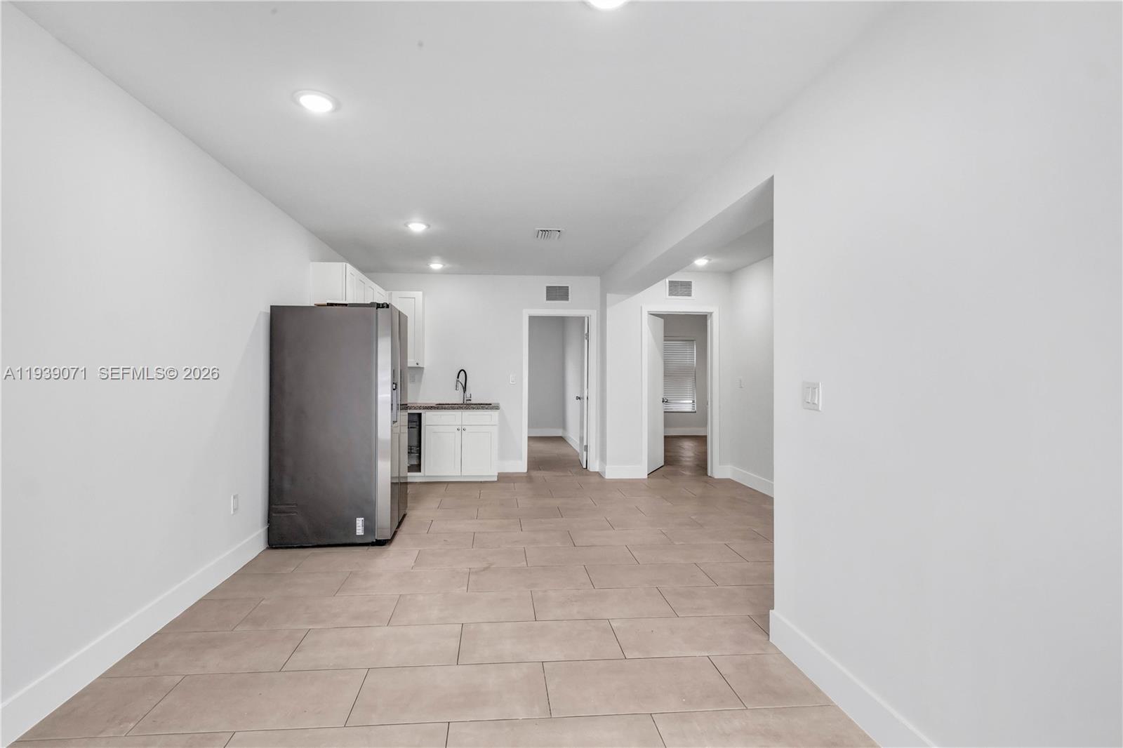 A kitchen area features a stainless steel refrigerator, white cabinetry, and light-colored tile flooring — 1749 NW 64th St # A, Miami FL 33147, MIAMI, FL