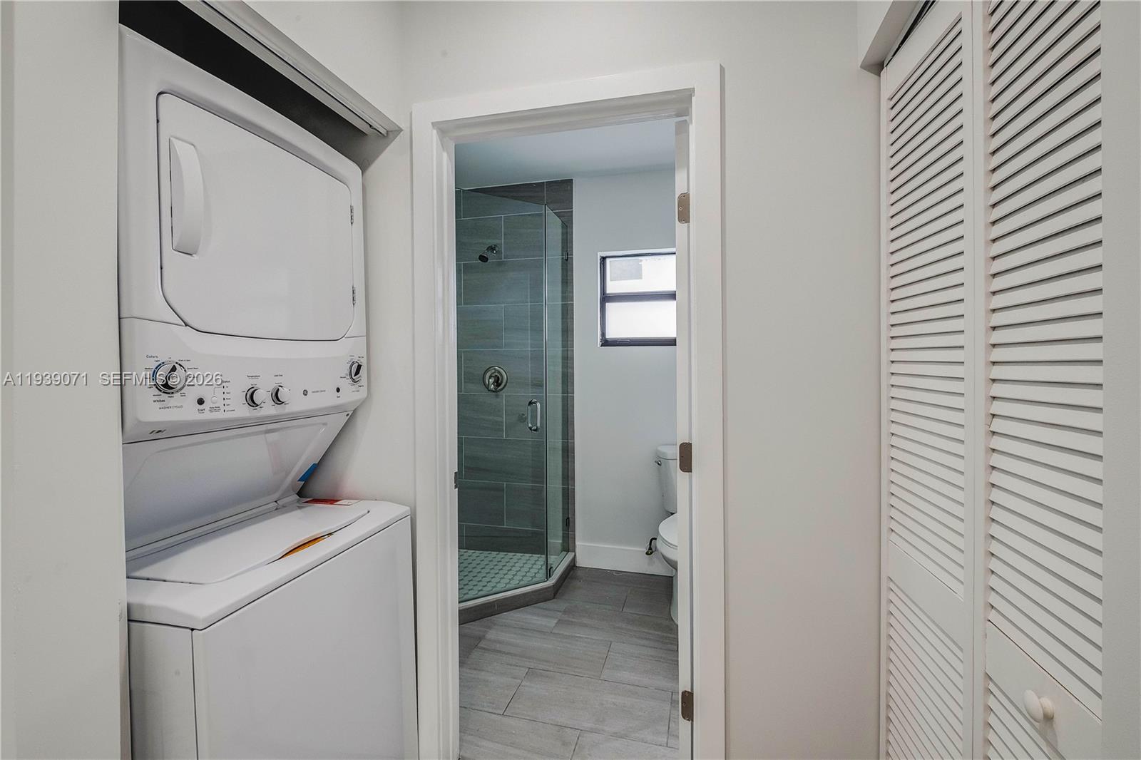 A laundry area with a stacked washer-dryer unit leads into a bathroom with a shower — 1749 NW 64th St # A, Miami FL 33147, MIAMI, FL