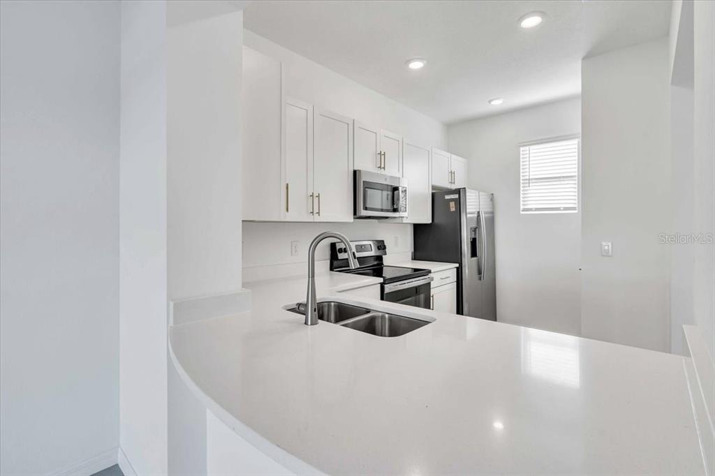 A modern kitchen features white cabinets, stainless steel appliances, and a white quartz countertop — 11747 STONESMITH CROSSING, PALMETTO, FL