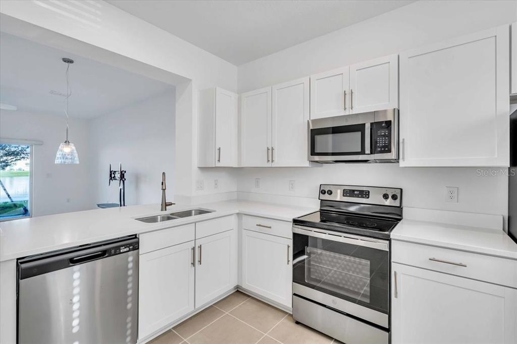A kitchen with white cabinets, stainless steel appliances, and a view into an adjacent room — 11747 STONESMITH CROSSING, PALMETTO, FL