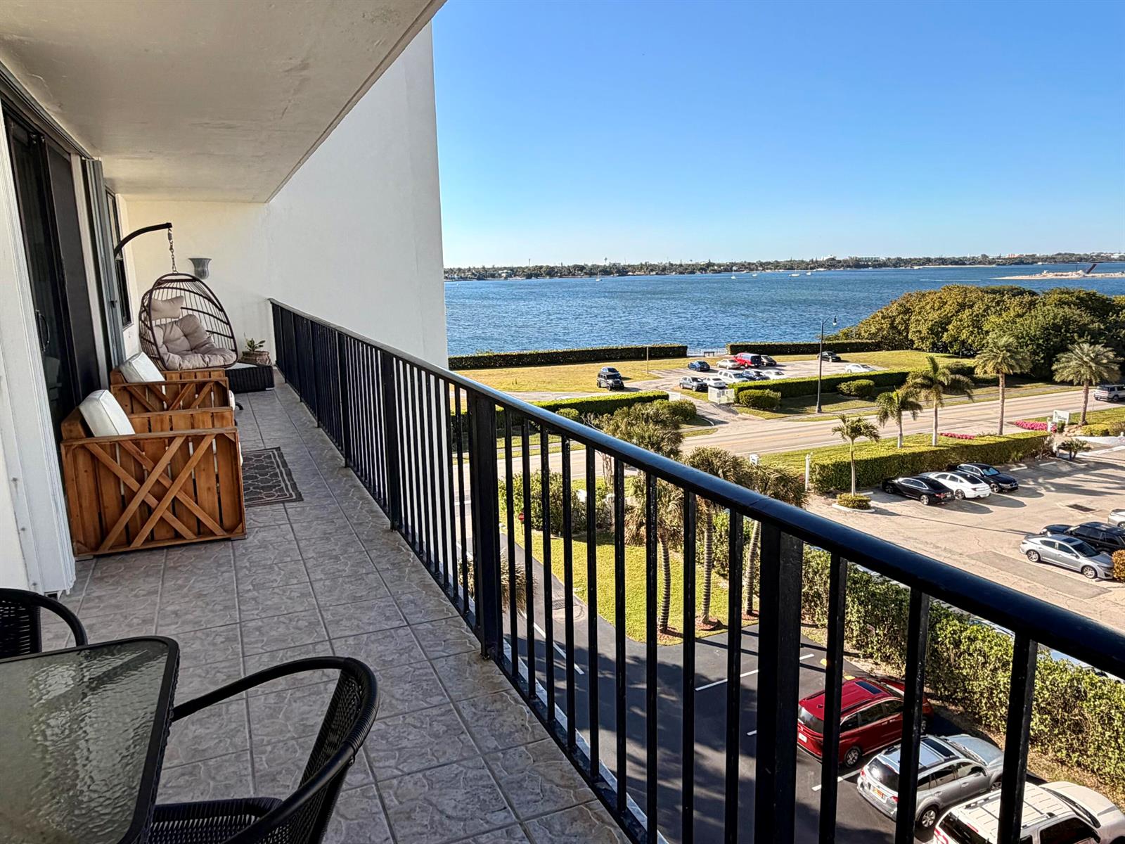 A balcony with patio furniture overlooks a parking lot, palm trees, and a large body of water — 3460 S Ocean Boulevard # 5110, Palm Beach FL 33480, PALM BEACH, FL
