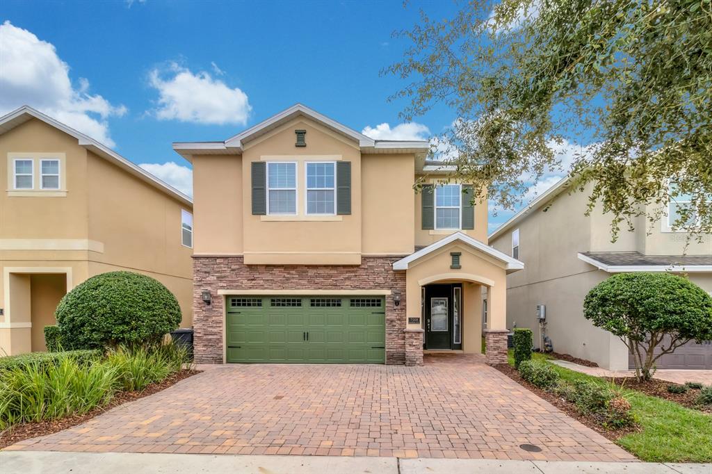 A two-story house features a green garage door, stone veneer accents, and a paved driveway — 7568 MARKER AVENUE, KISSIMMEE, FL