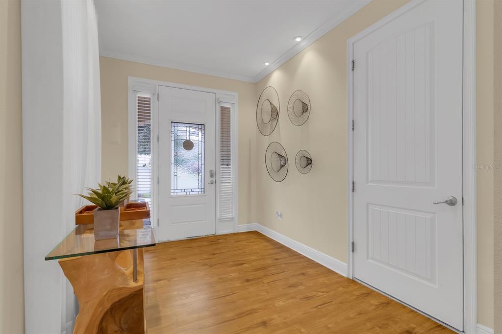 A bright entryway features wood-look flooring, a white front door, and a glass-topped console table — 7568 MARKER AVENUE, KISSIMMEE, FL