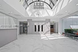 A bright, modern lobby features white marble floors, a glass skylight, and a reception desk — 1000 Brickell Ave # 11A, Miami FL 33131, MIAMI, FL