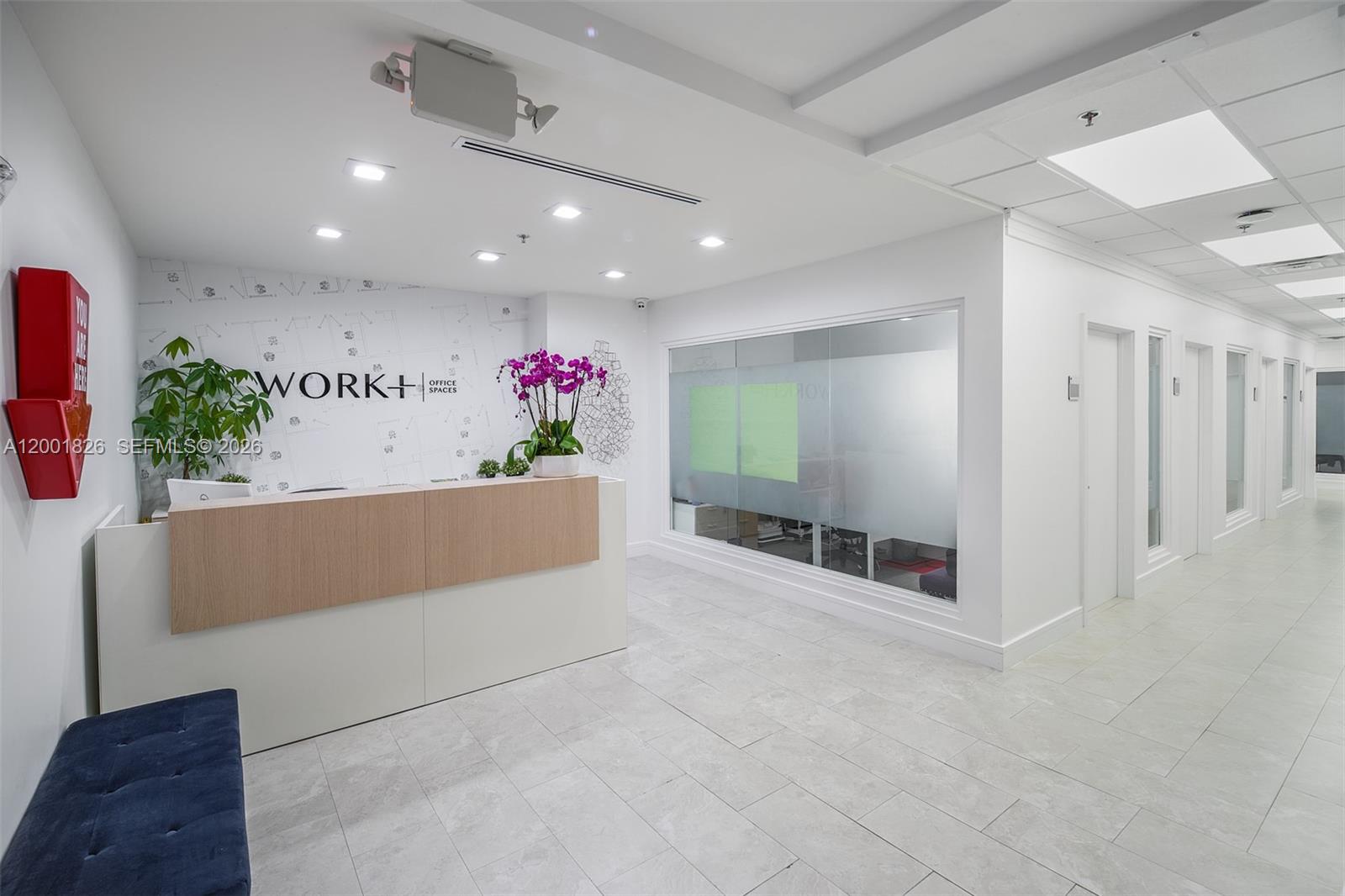 A modern office reception area features a wooden desk, white walls, and a glass-walled office — 1000 Brickell Ave # 11A, Miami FL 33131, MIAMI, FL