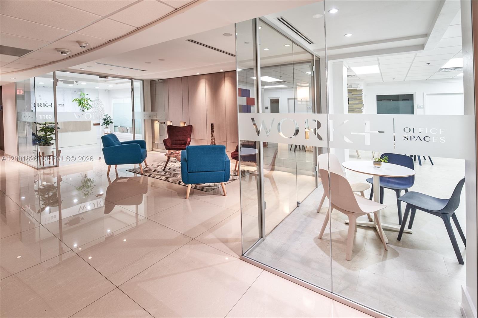 A modern office lobby features glass-walled meeting rooms, blue and maroon armchairs, and tiled flooring — 1000 Brickell Ave # 11A, Miami FL 33131, MIAMI, FL