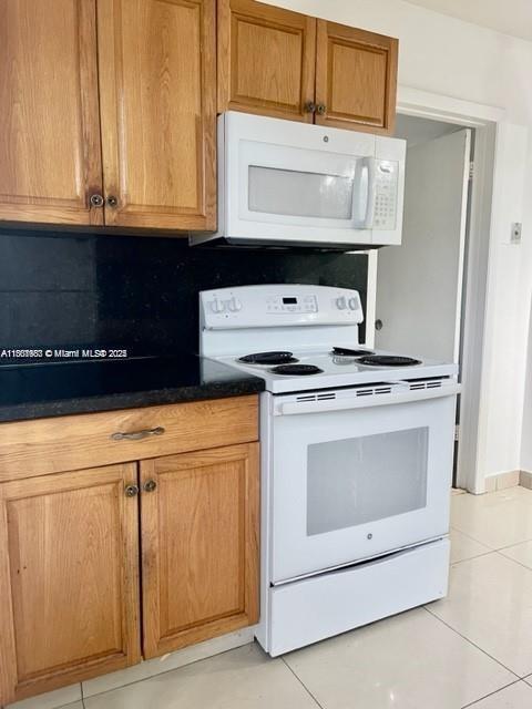 A kitchen features light wood cabinets, a white microwave, and a white electric range — 310 SW 10th Ter, Hallandale Beach FL 33009, HALLANDALE BEACH, FL