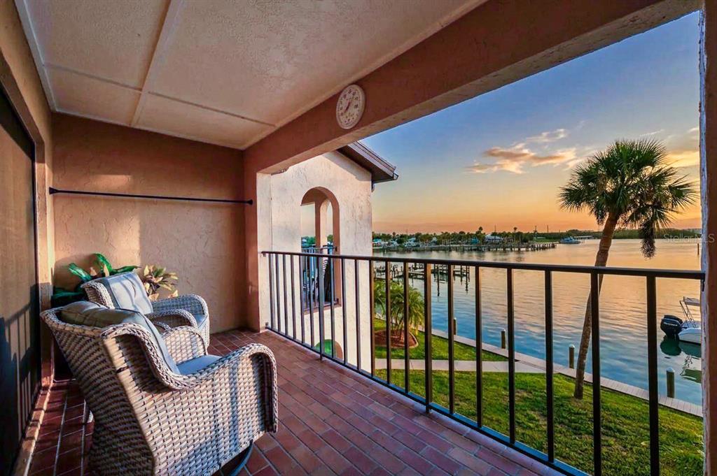 A balcony with wicker chairs overlooks a waterfront view at sunset — 1765 GULF BOULEVARD UNIT 203, ENGLEWOOD, FL