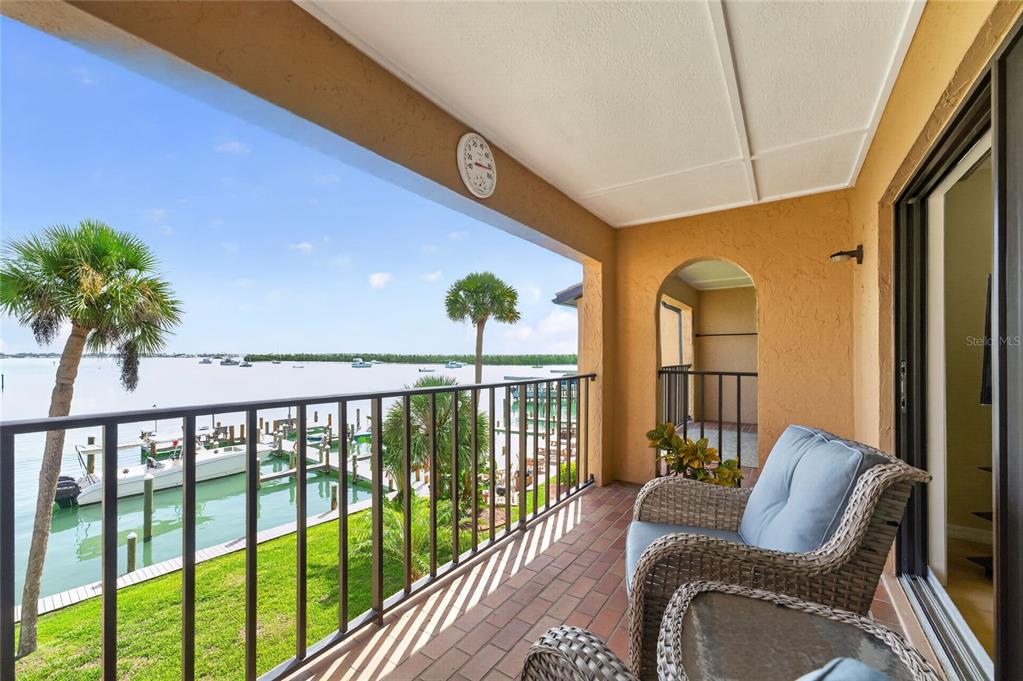 A covered balcony features wicker chairs, a brick floor, and a view of a marina — 1765 GULF BOULEVARD UNIT 203, ENGLEWOOD, FL