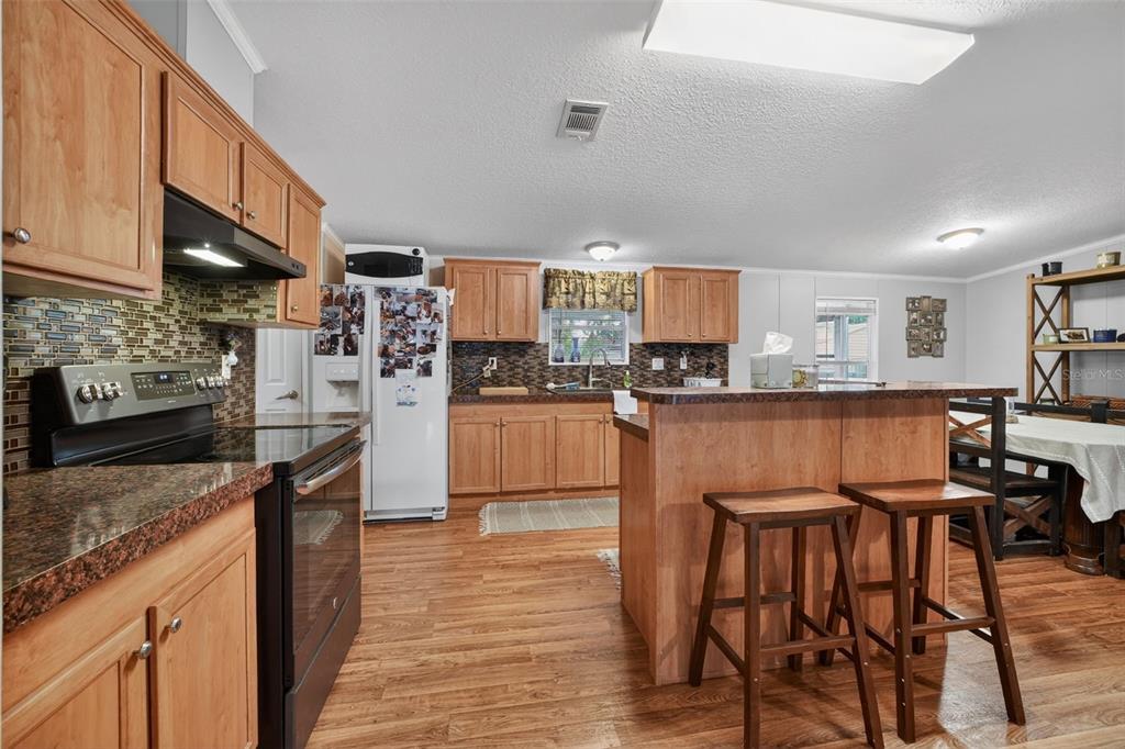 A kitchen with wood cabinets, a granite-topped island, and wood-look flooring — 163 WEST STREET, OAK HILL, FL