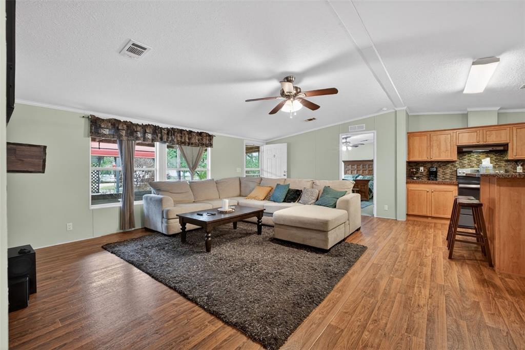A living room with wood-look flooring, a sectional sofa, and an open kitchen area — 163 WEST STREET, OAK HILL, FL