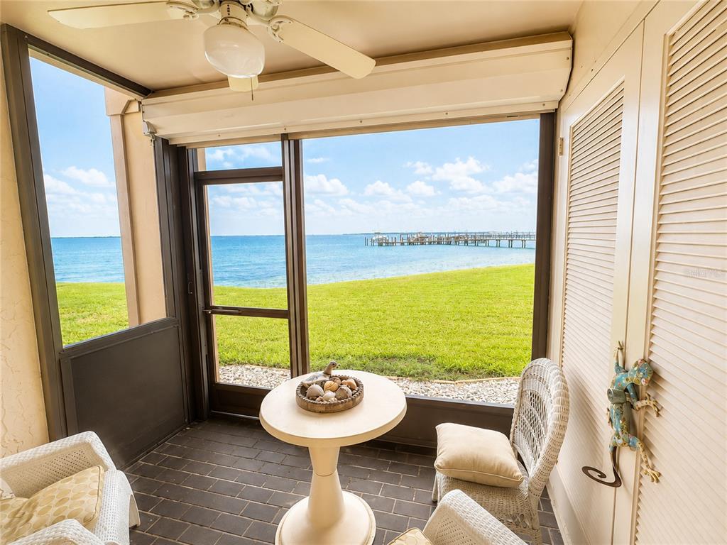 A screened-in porch features wicker furniture, a small table, and a view of the water — 6051 SUN BOULEVARD UNIT 111, ST PETERSBURG, FL