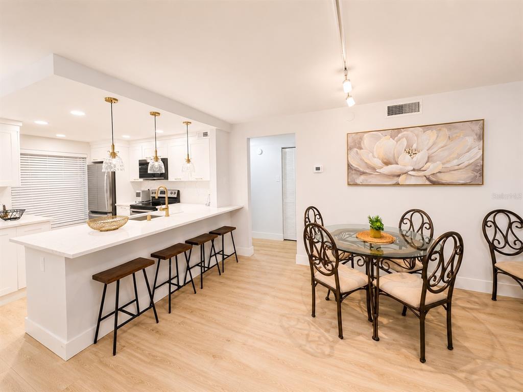 A kitchen with a breakfast bar and stools next to a dining area with chairs — 6051 SUN BOULEVARD UNIT 111, ST PETERSBURG, FL