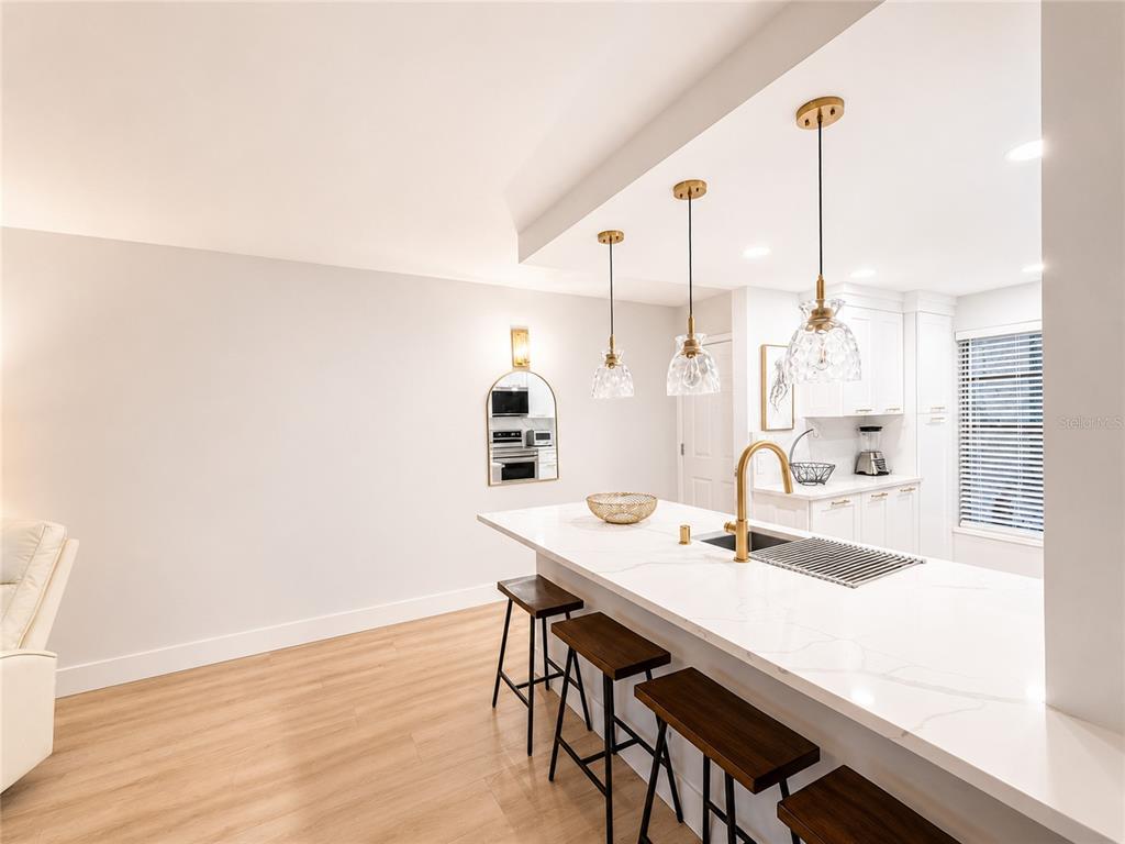 A kitchen features a white quartz island with bar seating, gold fixtures, and pendant lighting — 6051 SUN BOULEVARD UNIT 111, ST PETERSBURG, FL