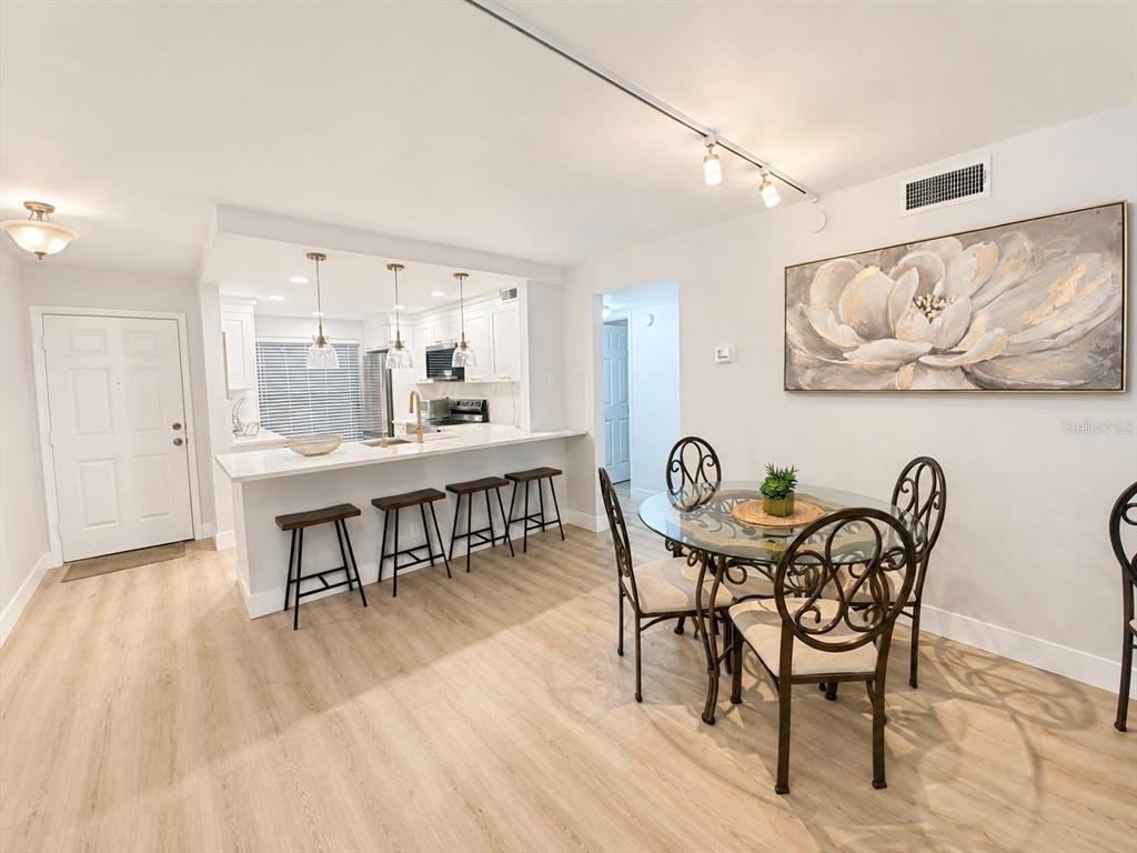 A kitchen with a breakfast bar and stools sits adjacent to a glass-topped dining table — 6051 SUN BOULEVARD UNIT 111, ST PETERSBURG, FL