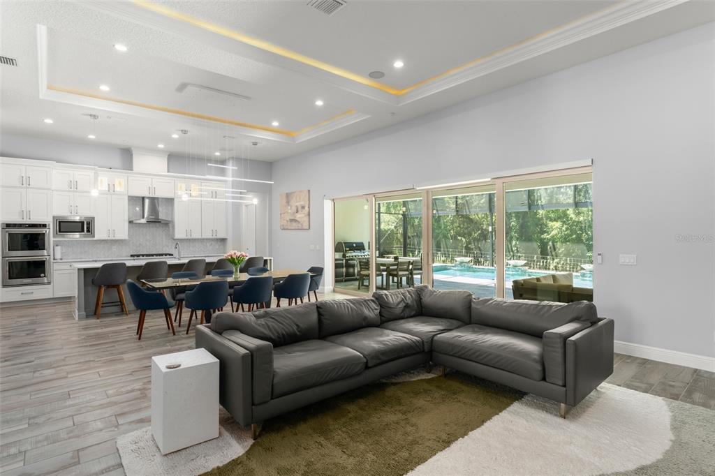 An open-concept living and dining area features a large sectional, modern kitchen, and sliding glass doors — 15619 GIANT FOXTAIL COURT, WINTER GARDEN, FL