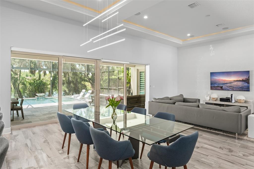 A dining area with a glass table and blue chairs opens to a pool patio — 15619 GIANT FOXTAIL COURT, WINTER GARDEN, FL