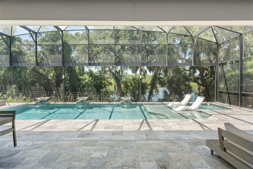 A screened-in pool area features stone decking, water fountains, and a view of trees — 15619 GIANT FOXTAIL COURT, WINTER GARDEN, FL