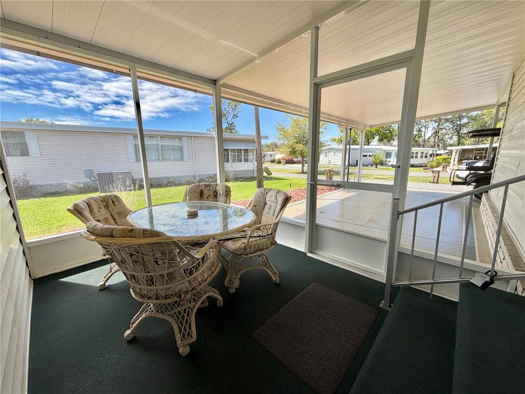 A screened-in porch features a glass-topped wicker dining set, green carpeting, and metal stairs — 325 PALO VERDE DRIVE, LEESBURG, FL