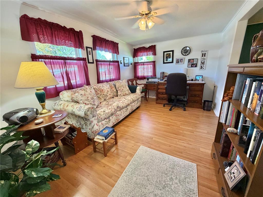 A home office features a floral sofa, wooden desk, and hardwood floors under a ceiling fan — 325 PALO VERDE DRIVE, LEESBURG, FL