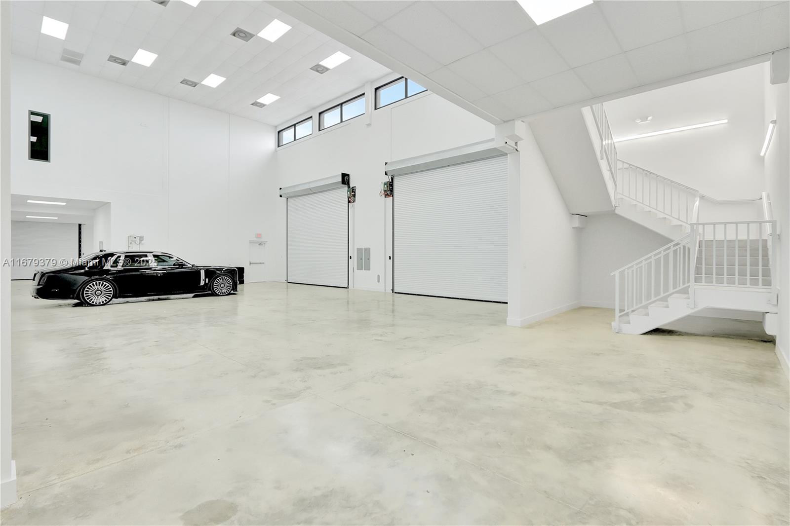 A spacious, white-walled industrial warehouse space features a black luxury car and a staircase — 6700 NE 2nd Ct # 4, Miami FL 33138, MIAMI, FL