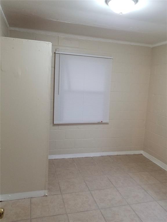 A room with light-colored tile flooring, painted concrete block walls, and a window with blinds — 1809 SW 3RD STREET, OCALA, FL