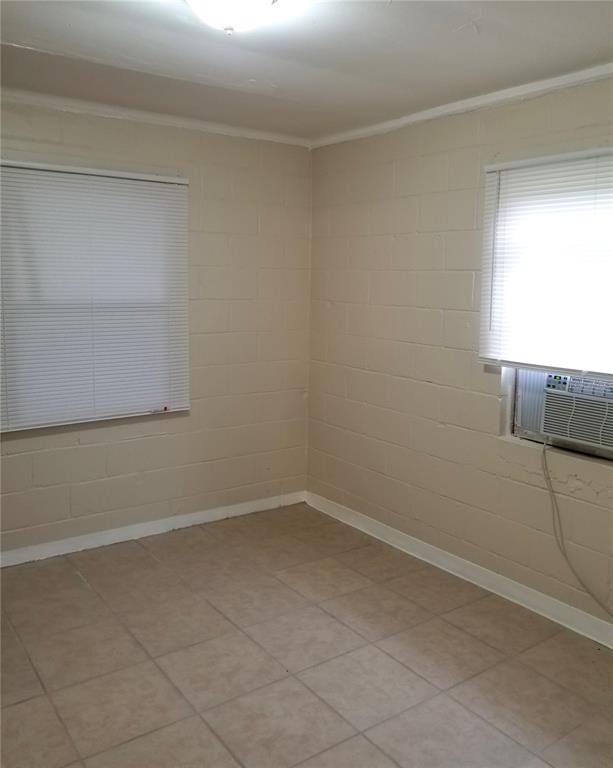 An empty room features beige painted concrete block walls, tiled flooring, and two windows — 1809 SW 3RD STREET, OCALA, FL