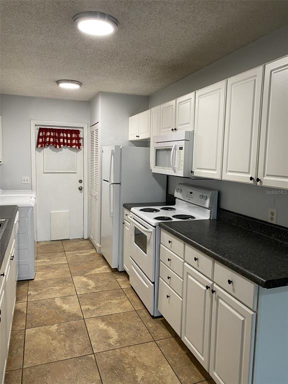 A kitchen features white cabinets, black countertops, white appliances, and tan tile flooring — 12310 TAVARES RIDGE COURT UNIT 144, TAVARES, FL