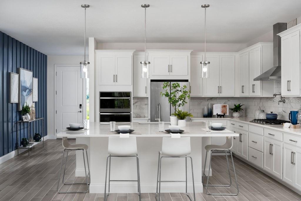 A modern kitchen features white cabinetry, a large central island with bar seating, and blue walls — 2366 WISE RIVER LANE, ZEPHYRHILLS, FL