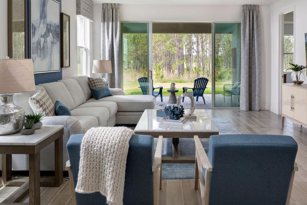 A living room with a sectional sofa, blue armchairs, and sliding doors opening to a patio — 2366 WISE RIVER LANE, ZEPHYRHILLS, FL
