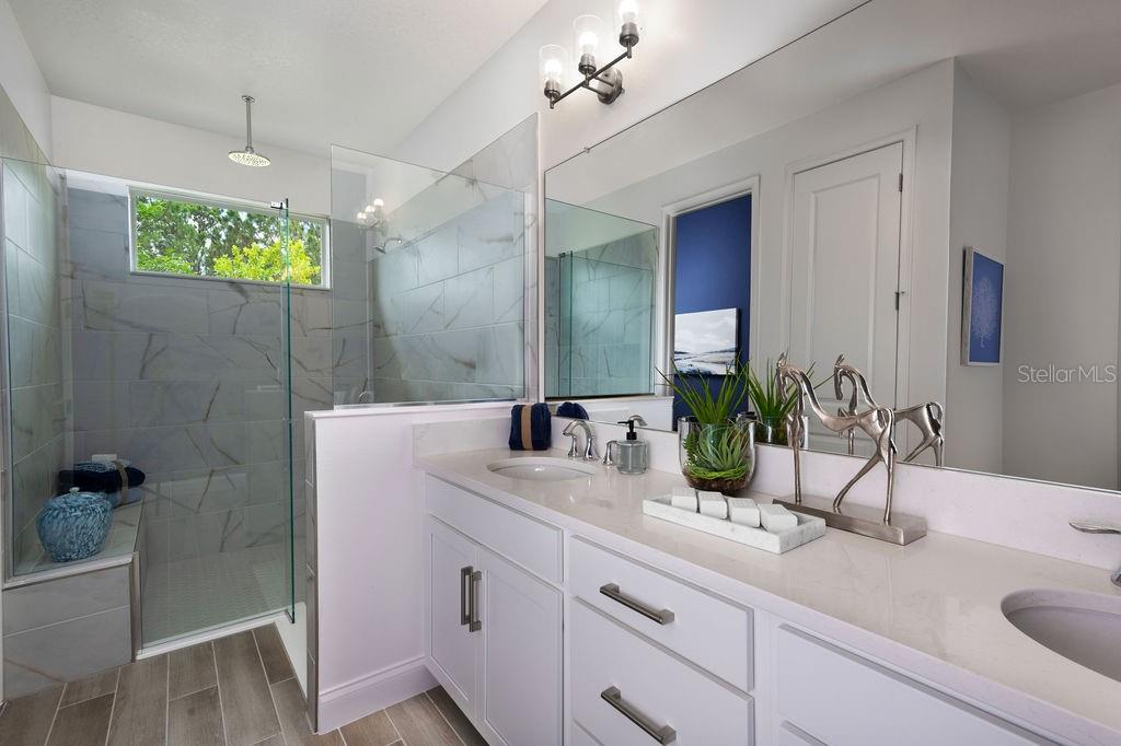 A modern bathroom features a white double vanity, a glass-enclosed walk-in shower, and marble-look tile — 2366 WISE RIVER LANE, ZEPHYRHILLS, FL