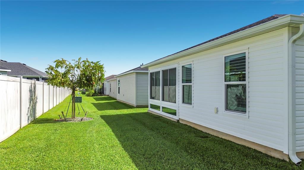 The side yard of a house features a white vinyl fence, a small tree, and a screened-in porch — 6966 LISA LANE, THE VILLAGES, FL