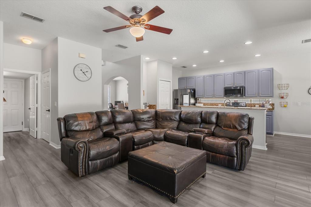 A living room with a large brown leather sectional, ottoman, and an open kitchen — 9361 PECKY CYPRESS WAY, ORLANDO, FL