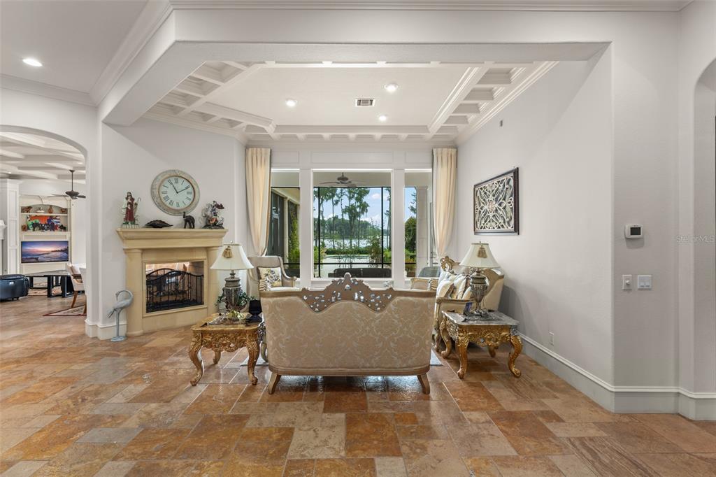 A living room features a stone fireplace, ornate furniture, tile flooring, and large windows overlooking water — 6055 LOUISE COVE DRIVE, WINDERMERE, FL