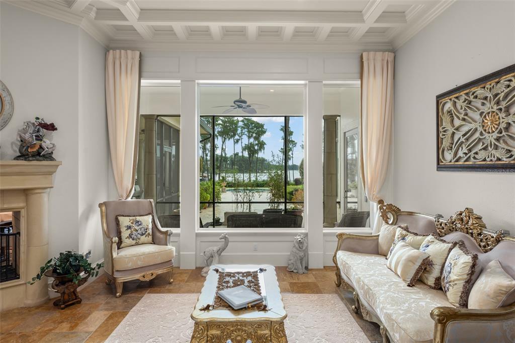 A formal living room features ornate furniture, a coffered ceiling, and large windows overlooking a lake — 6055 LOUISE COVE DRIVE, WINDERMERE, FL