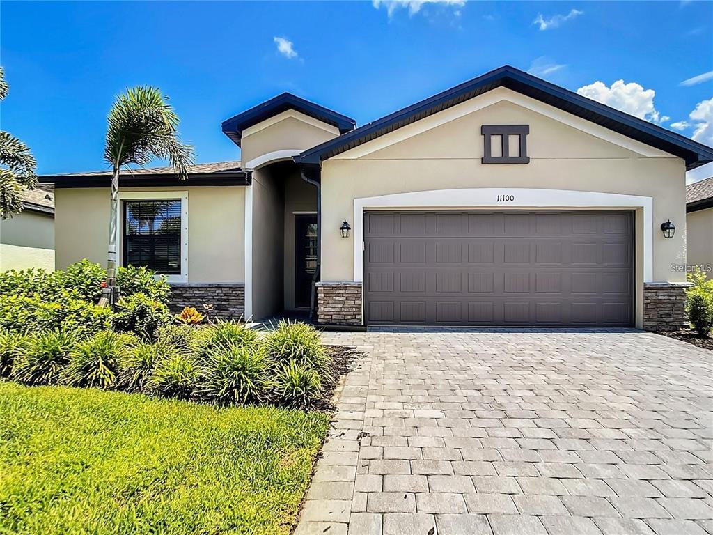 A single-story house exterior features a beige stucco facade, a stone base, and a paved driveway — 11100 BALFOUR STREET, VENICE, FL