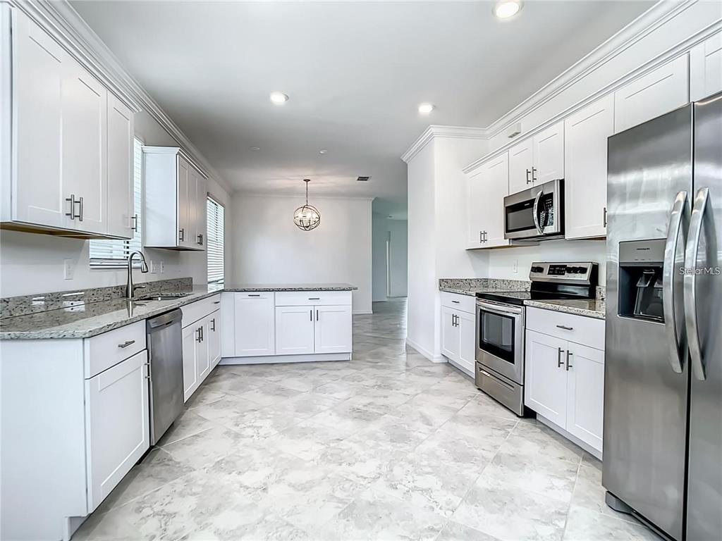 A kitchen features white cabinets, stainless steel appliances, granite countertops, and light-colored tile flooring — 11100 BALFOUR STREET, VENICE, FL