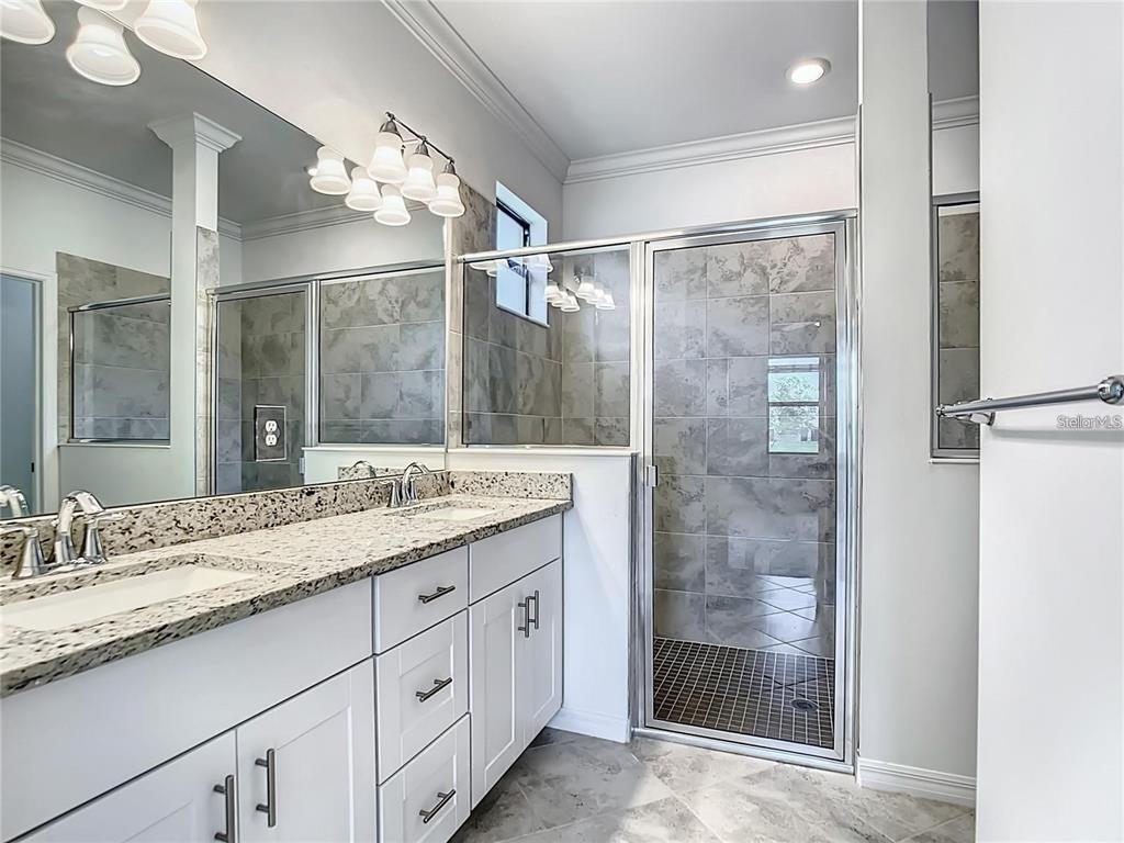 A bathroom features a double vanity with granite countertops, white cabinets, and a glass-enclosed shower — 11100 BALFOUR STREET, VENICE, FL